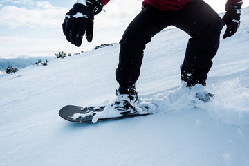 cropped view of snowboarder in gloves riding on slope with white snow in wintertime