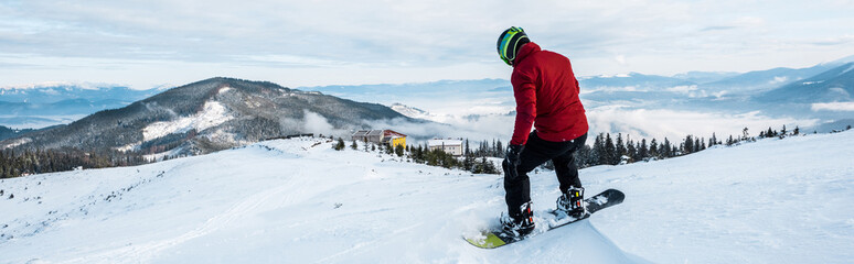 panoramic shot of snowboarder in helmet riding on slope in wintertime