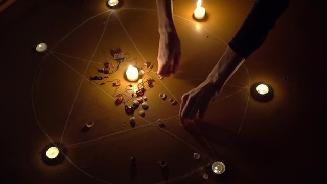 A female hand collects shells and stones, white candles burn in a pentagram on a wooden floor. Magical ritual with occult, evil and esoteric symbols. Halloween Scary Rite