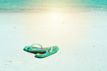 Closeup pair of old sandals put on the white sand beach with blurred sea surfing into the coast background