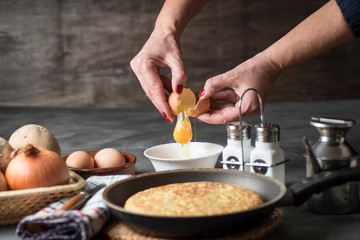 Spanish potato omelette, on a table, next to the necessary ingredients to be cooked and ready to be eaten