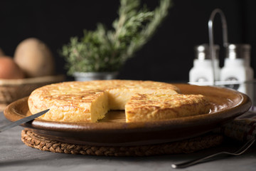 Spanish potato omelette, on a table, next to the necessary ingredients to be cooked and ready to be eaten