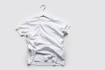 Flatlay with white t-shirt on white hanger on white background.