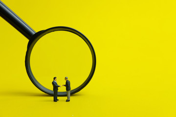 Miniature people, partnership concept - two businessman make a handshake in front of magnifier...