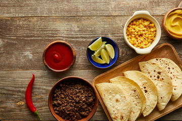 Top view of fresh tortillas with sauces and ingredients on wooden background