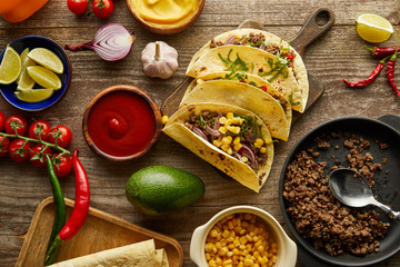 Top view of cooked tacos with vegetables and sauces on wooden surface