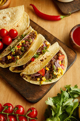 Top view of tacos on cutting board with ripe vegetables on wooden table
