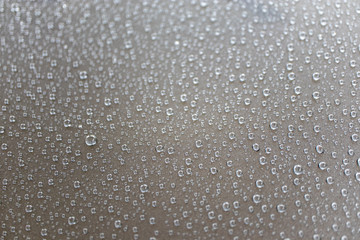 The dew is on the hood of a dark gray car on a rainy day