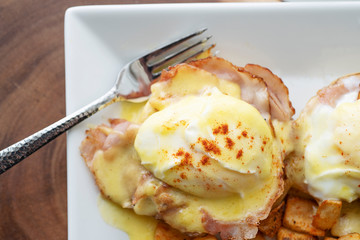 Up close eggs Benedict with a fork on a white plate