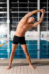 handsome swimmer in swimming cap warming up near swimming pool