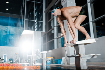 shirtless swimmer standing in starting pose on diving block