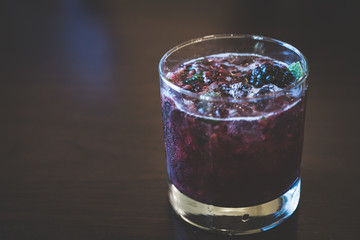 glass blackberry and mint cocktail with ice on wood background