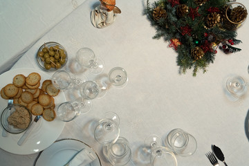 Fototapeta na wymiar Christmas table with a white tablecloth, crystal glasses, pieces of cutlery and christmas decoration.