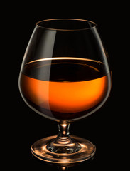 Snifter glass with cognac, brandy on a reflective surface on dark background.