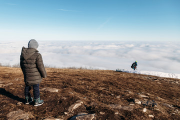 people at the top of the mountain take pictures of paragliders and beautiful views above the clouds