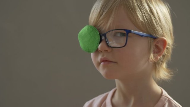 Portrait of funny child in new glasses with green spot to correct strabismus Orthopedic Boys Eye Patches nozzle for glasses for treatment of strabismus (lazy eye). Boy puts on and corrects glasses