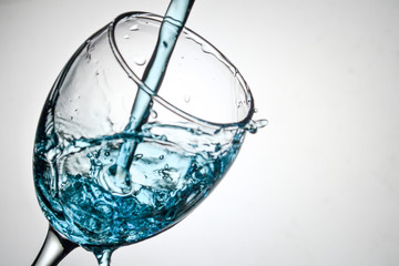 Stream of blue water pouring into a transparent glass with splashes