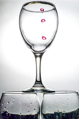 Drops of red wine falling into a transparent glass with splashes