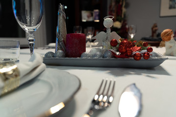 Christmas table with a white tablecloth, crystal glasses, pieces of cutlery, red candles and christmas decoration.