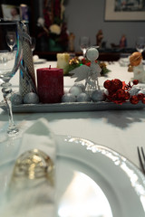 Christmas table with a white tablecloth, crystal glasses, pieces of cutlery, red candles and christmas decoration.