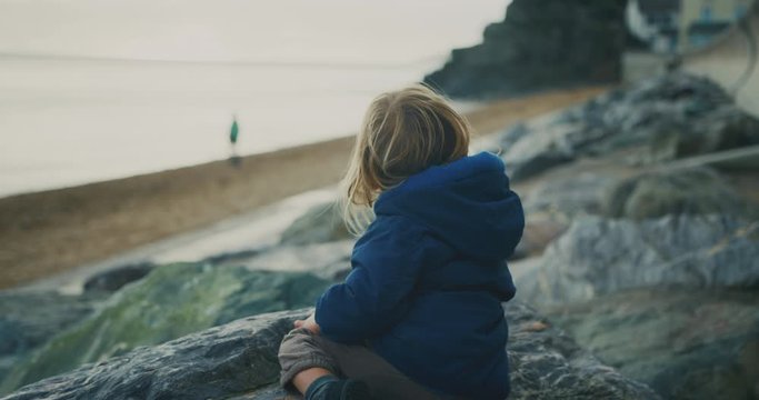 Little toddler sitting on rocks by the beach in winter