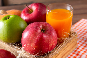 apples in a box, a glass of juice on a wooden background, fresh fruit