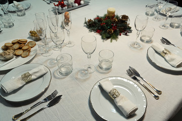 Christmas table with a white tablecloth, crystal glasses, pieces of cutlery, red candles and christmas decoration.