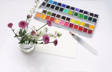Flower with watercolors, brush and palette on white paper background.
