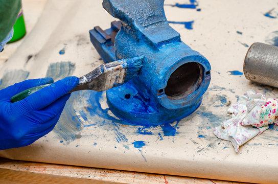 Worker paints a metal vise with blue paint. Stripping old paint