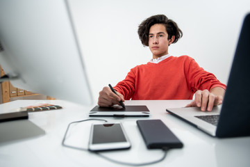 Young serious web designer using laptop while looking at computer screen