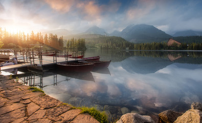 Fototapeta na wymiar A wonderful Colorful Sunset at lake Strbske pleso, in High Tatra. Picturesque Dramatic sky glowing in sunlight, over the Fairytale calm lake. Scenic image of woodland in sunlit. Autumn Landscape