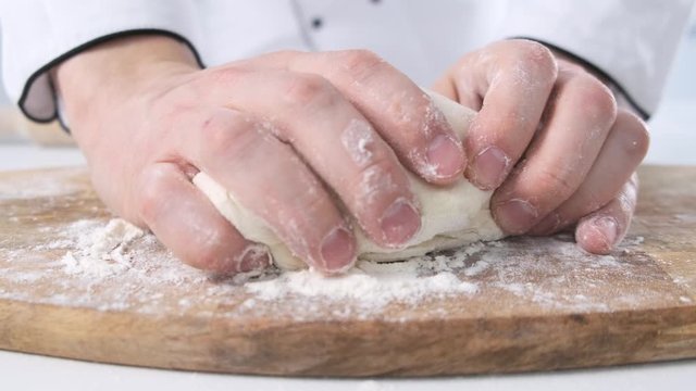 Male hands kneading dough in flour on a table and wooden board. Close up.