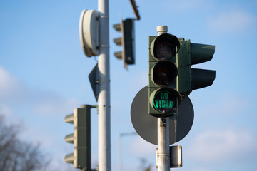 Germany, Berlin green traffic light, signal with special label shows go vegan, blue sky, clouds and tree in background 