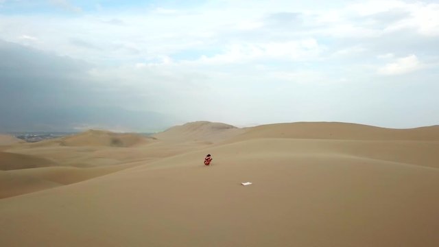 Aerial, orbit, drone shot, around a girl taking pictures, on sand dunes, at the Atacama desert, on a sunny day, in south Peru