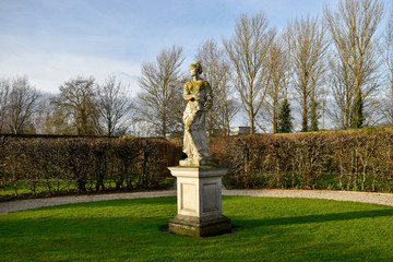 A sculpture of a woman in a european garden which can be seen in the background. Great for use as a concept to describe european culture and history