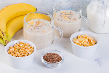 Banana smoothie in cups, flax seeds, cocoa, oatmeal and puffed rice on a white background. Healthy eating concept