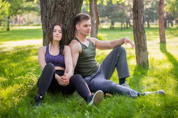 Athletic guy and girl sitting on the lawn leaning against a tree.