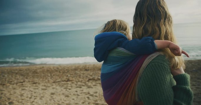 Young mother carrying her toddler in a sling on her back at the beach