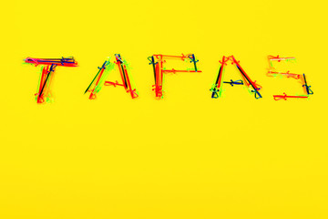 On yellow background is inscription Tapas, which is made of many multi-colored cocktail skewers. Such skewers are used to hold ingredients together in preparation of tapas. Copy space.