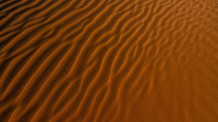 Red sand background with shadows from sunset sun, shot in desert at summer evening. Tourist attraction. 