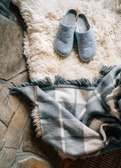 The pair of gray home slippers on the natural white sheep sheepskin with warm plaid dropped on the...