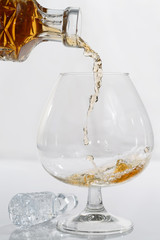 Pouring brandy from a crystal decanter into a snifter glass on white background