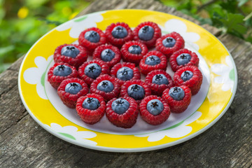 Lots of fresh raspberries inside with blueberries closeup on a yellow plate top view