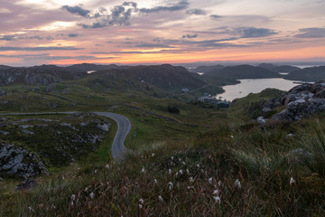 road through the mountains with sunset and lake.