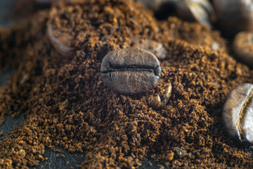 Coffee bean lies on ground coffee. Conceptual photo. Close-up on a black texture background.