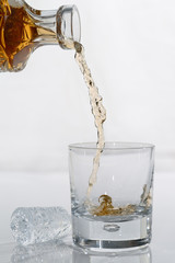 Pouring whiskey from a crystal decanter into a tumbler glass on white background