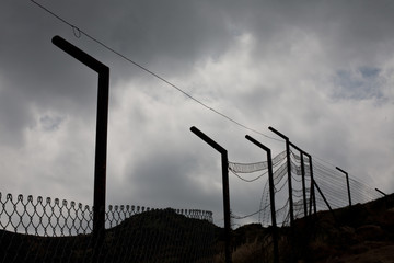Fototapeta premium Security fence in silhouette against cloudy sky in park