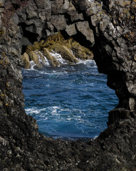 Hole in icelandic black lava rock formation with atlantic ocean in background.