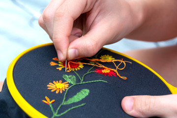 Women's hand embroidery in a hoop, a woman embroider a pattern on dark material. Close-up. The concept of needlework, hobby, leisure.