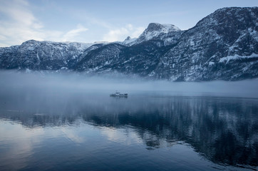 a ferry on the lake  passing by the foggy mountains with snow on the trees in winter